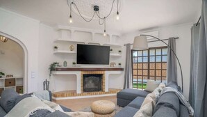 A modern living room with a fireplace, a large flat-screen TV, and a comfortable seating area. - Spacious House | Terrace & Pool by Host Wise (Lagoa)