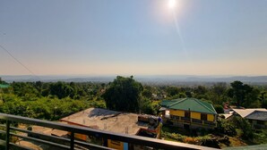 A view of a residential area with a green-roofed building and a yellow building with a sign that reads "Athbiga Cement." - Hotel JK Dharamshala (Dharamshala)