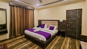 A hotel room with a large bed, wooden flooring, a ceiling fan, and a wardrobe. - Hotel JK Dharamshala (Dharamshala)