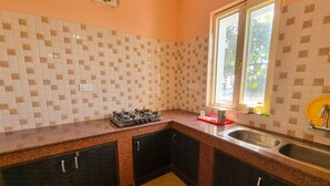 A kitchen with a gas stove, two sinks, dark cabinets, and a window with a view of greenery. - Hotel JK Dharamshala (Dharamshala)