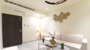 A modern, well-lit room with a sofa, two round tables, and decorative wall art. - Hotel Rudra Inn  (Bakshi Ka Talab)