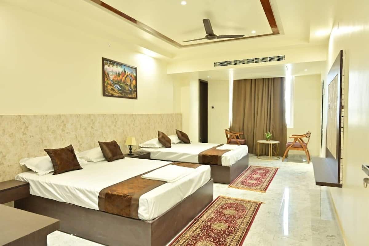 A hotel room with two beds, a ceiling fan, a painting, a small table, a chair, and a carpeted floor.