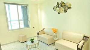 A living room with a beige sofa, a small round table with a plant, and a decorative wall piece. - Hotel Rudra Inn  (Bakshi Ka Talab)