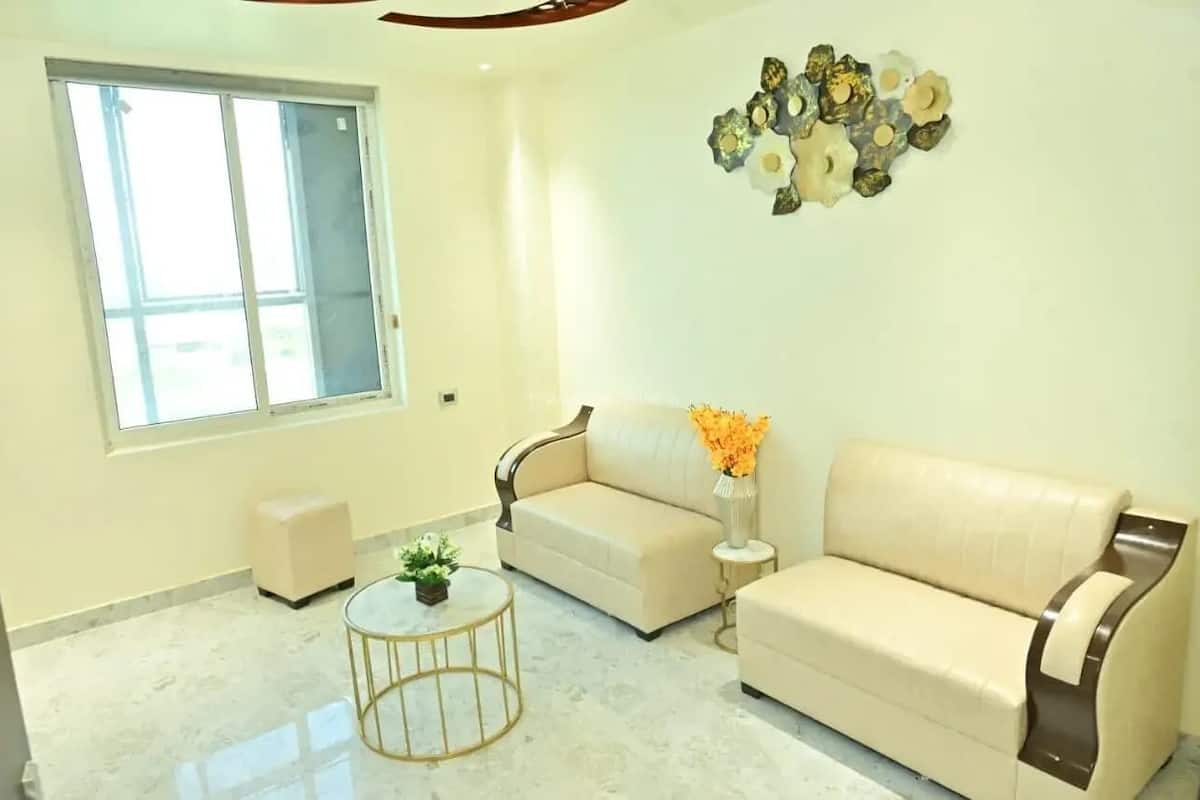 A living room with a beige sofa, a small round table with a plant, and a decorative wall piece.