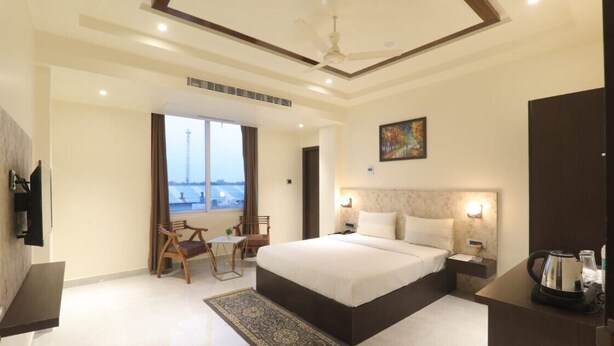 A modern hotel room with a large bed, a desk, a chair, and a view of a cityscape through the window. - Hotel Rudra Inn  (Bakshi Ka Talab)