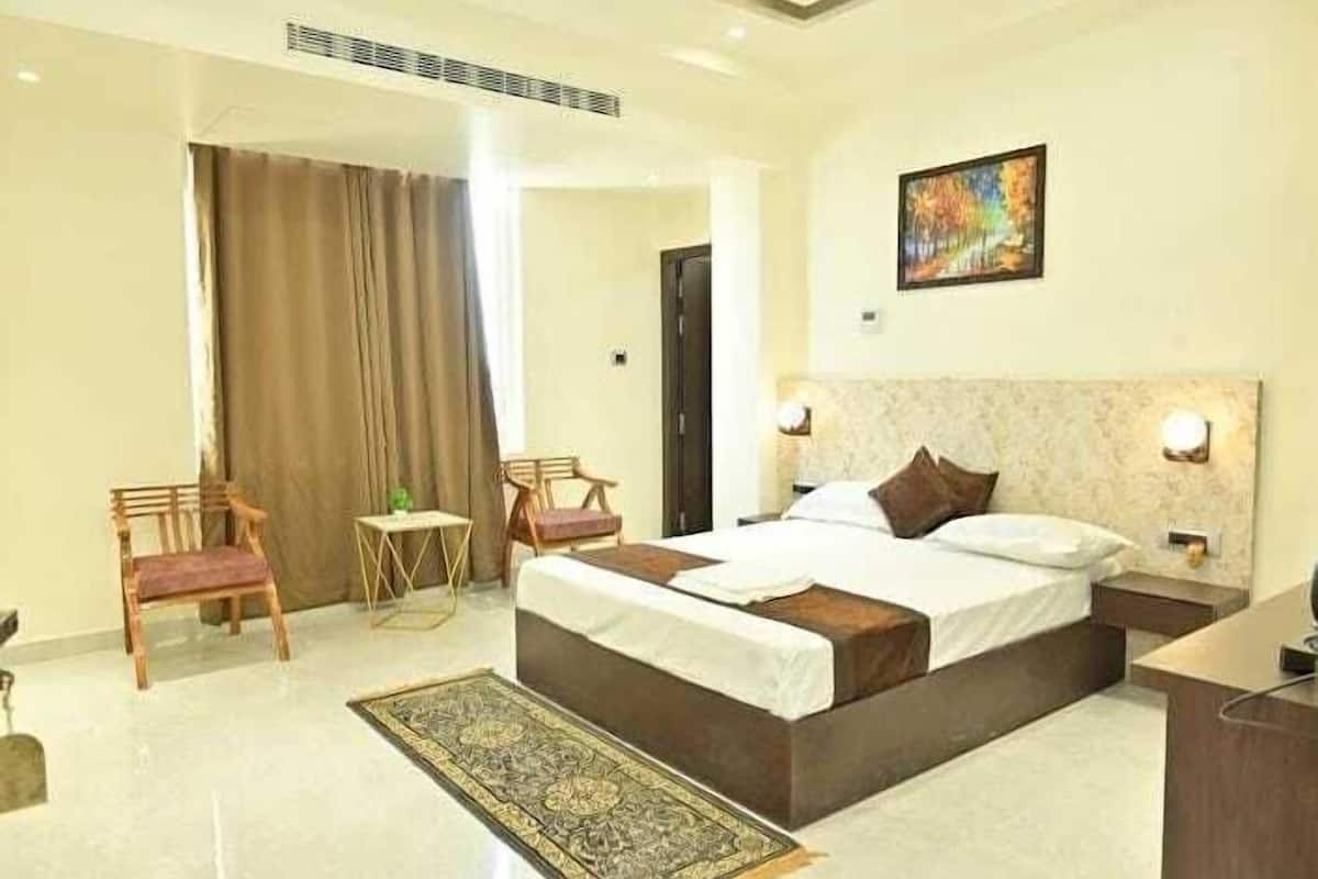 A hotel room with a large bed, two bedside tables, a nightstand, a chair, a small table, and a painting on the wall.