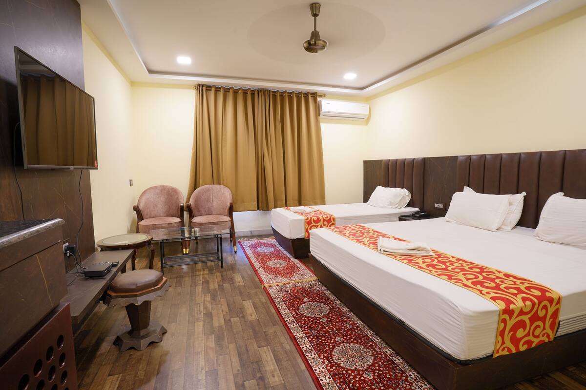A hotel room with a large bed, a desk with a chair, a TV mounted on the wall, and a window with curtains.