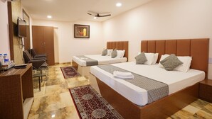 A hotel room with two beds, a desk, chairs, a TV, and a ceiling fan. - HOTEL TOURIST INN BY SAGAR (Siliguri)