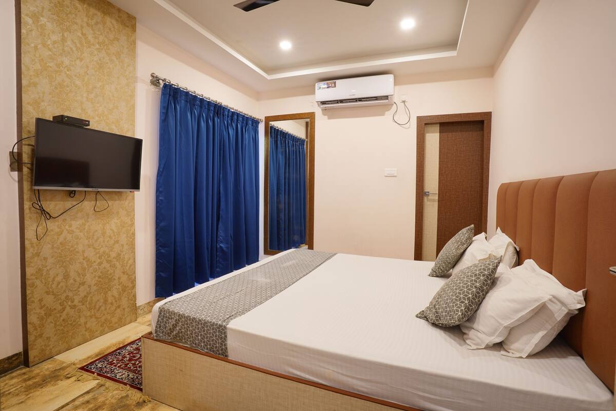A bedroom with a bed, a flat-screen TV, an air conditioning unit, and a mirror.
