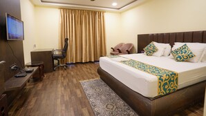 A hotel room with a bed, a desk, a chair, a television, and a ceiling fan. - HOTEL TOURIST INN BY SAGAR (Siliguri)