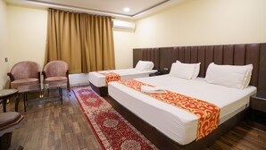 A hotel room with two beds, a sitting area with chairs, a glass table, a red and white patterned rug, and an air conditioning unit on the wall. - HOTEL TOURIST INN BY SAGAR (Siliguri)