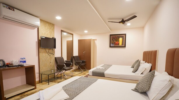 A hotel room with two beds, a desk, a chair, a TV, and a ceiling fan. - HOTEL TOURIST INN BY SAGAR (Siliguri)