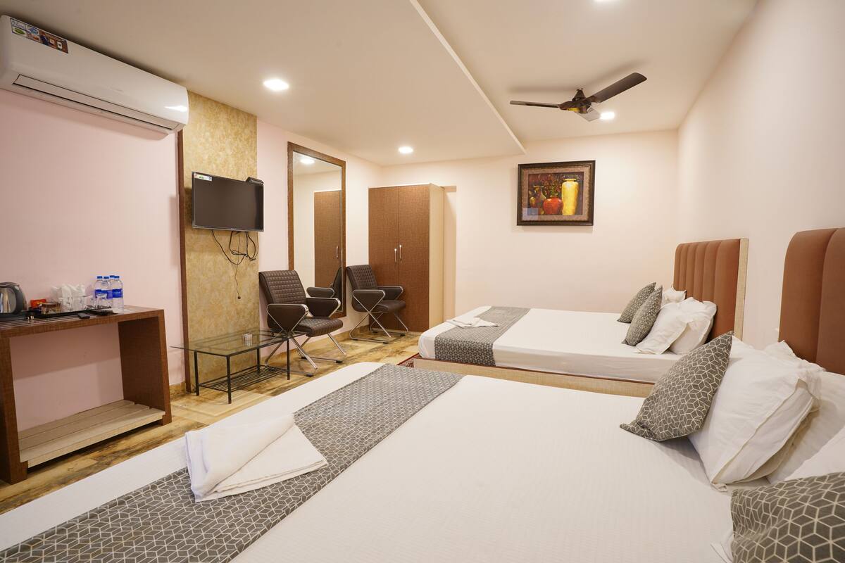 A hotel room with two beds, a desk, a chair, a TV, and a ceiling fan.