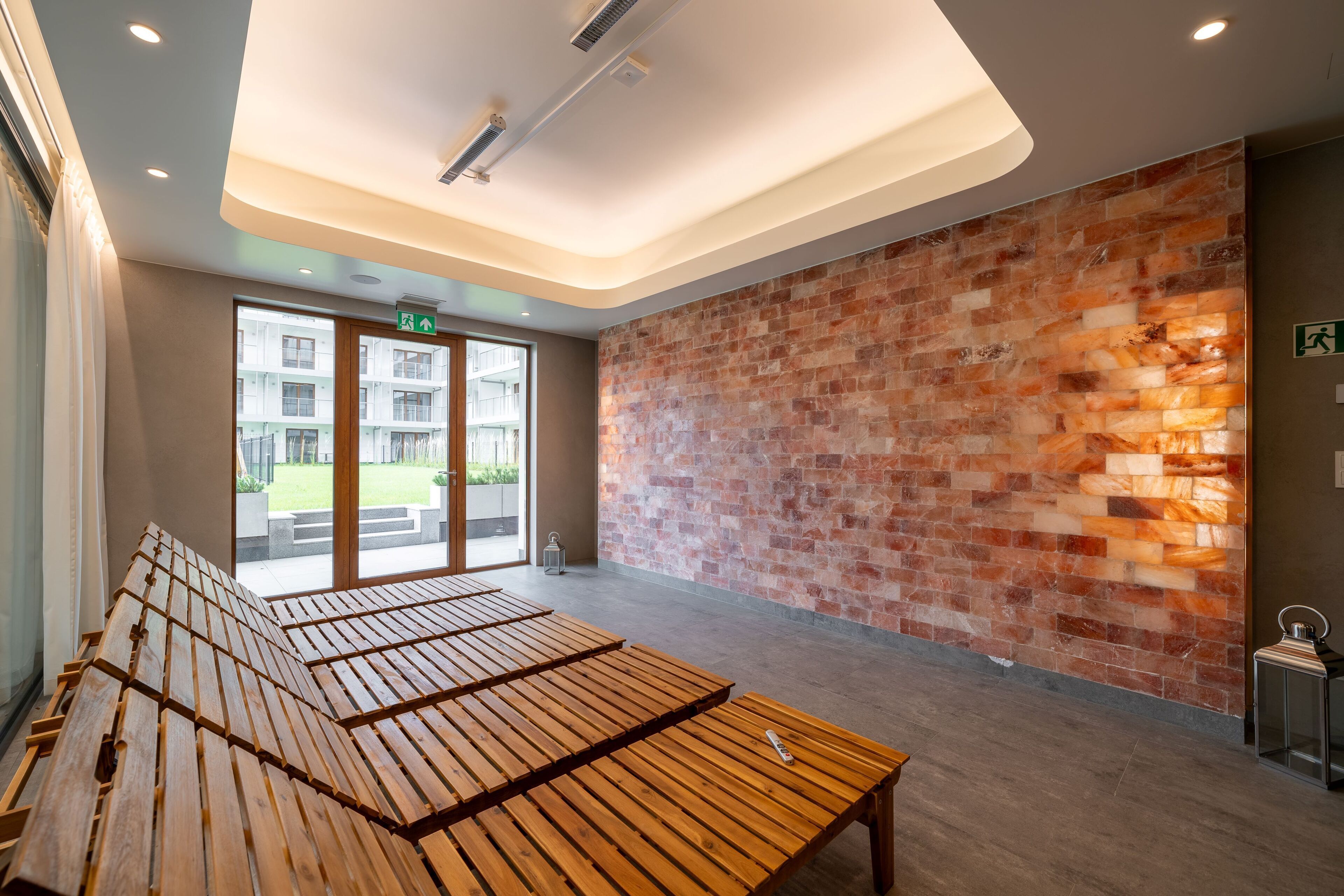 Un espace d’attente moderne avec des bancs en bois, un mur en briques et une porte en verre donnant sur l’extérieur.