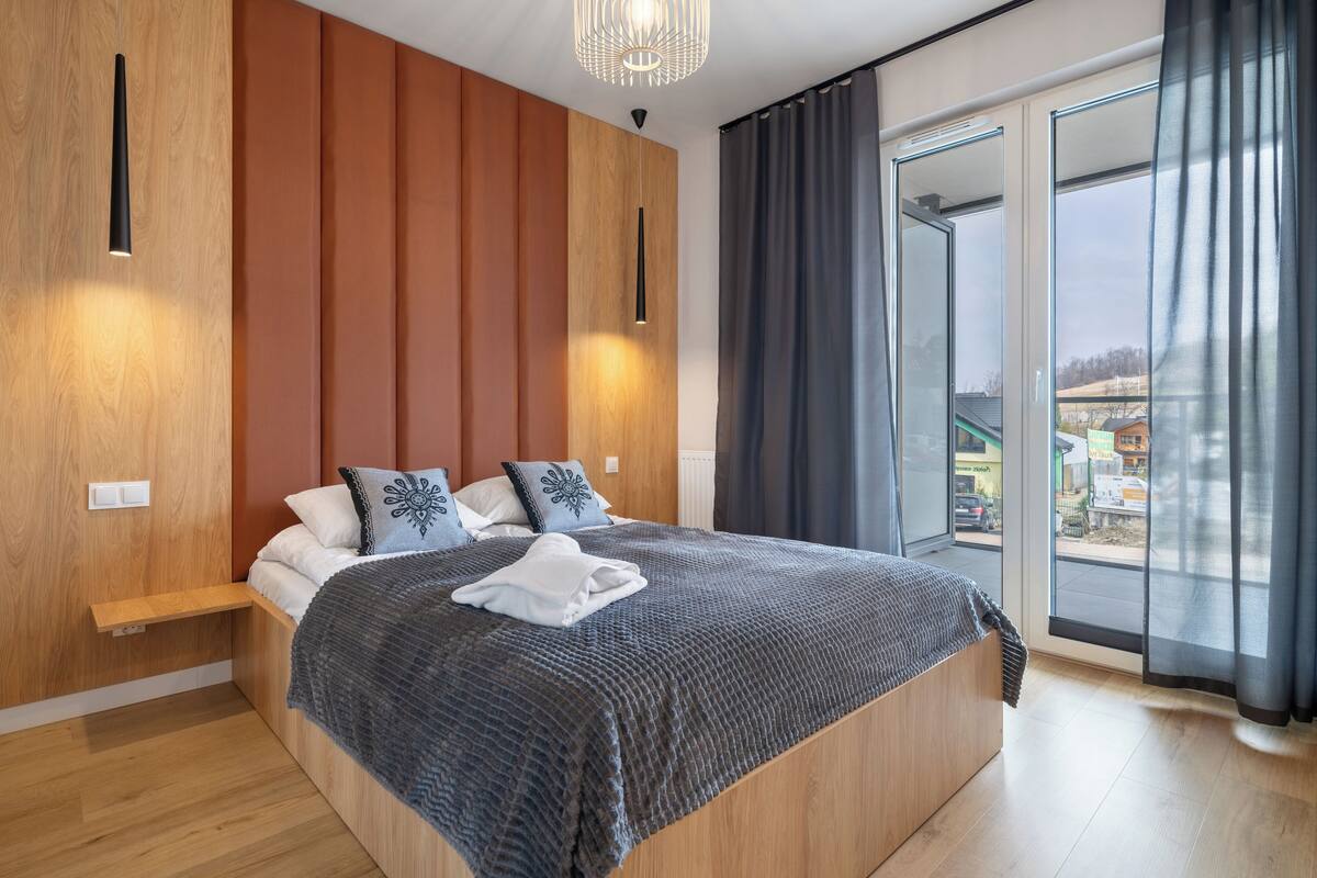 Un dormitorio moderno con una cama grande, paneles de madera, un banco empotrado y vistas a través de un ventanal amplio.