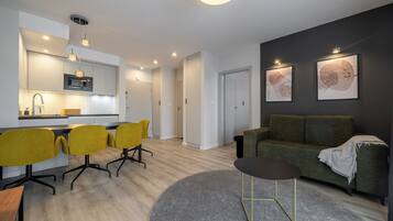A modern living room with a green sofa, yellow chairs, a round coffee table, and a kitchen area with a microwave.