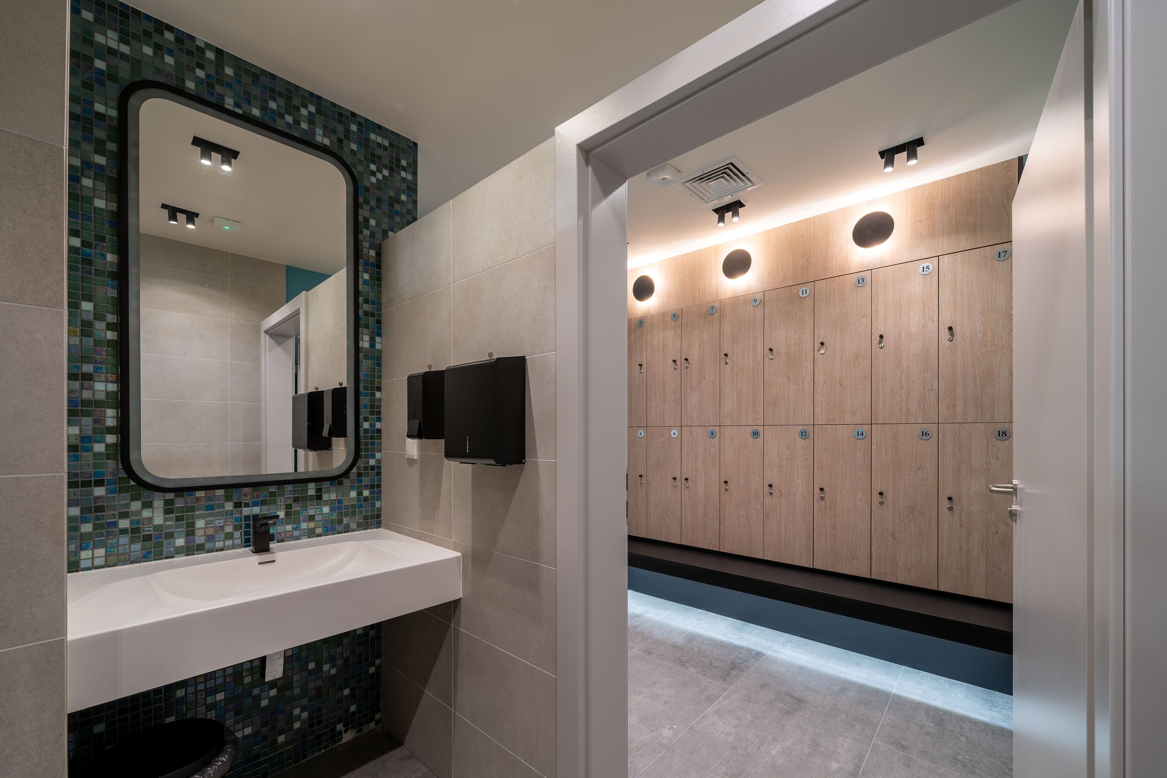 Un bagno moderno con un lavandino bianco, uno specchio con pannello decorativo a mosaico e armadietti in legno.