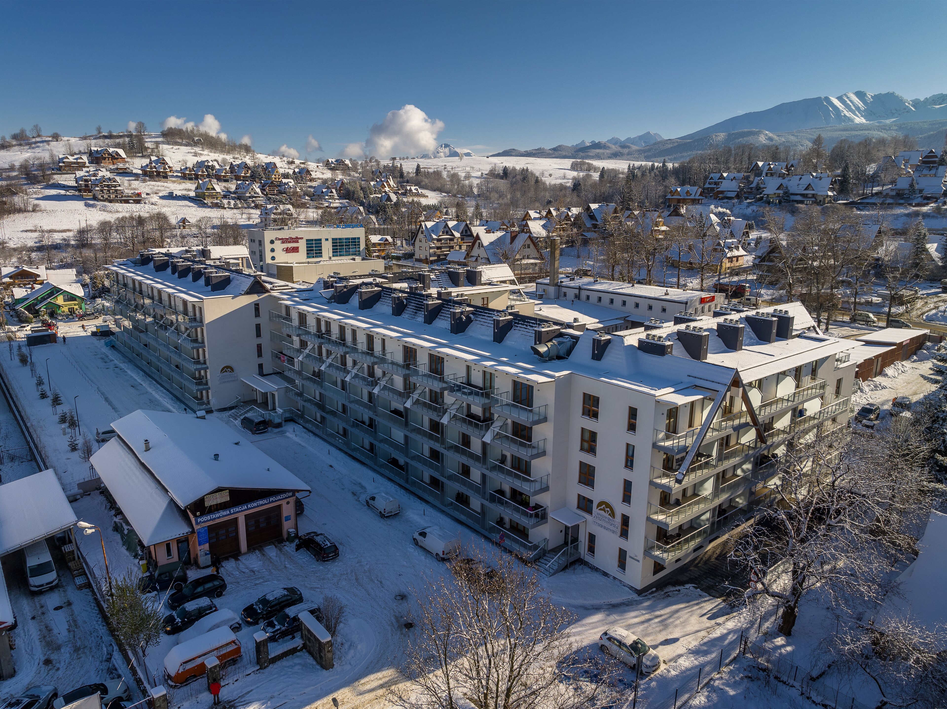 A hotel with multiple floors, a parking area, and a view of snow-covered mountains.