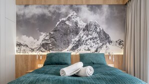 Quarto com um grande mural de montanhas, roupa de cama azul-turquesa e cabeceira de madeira.