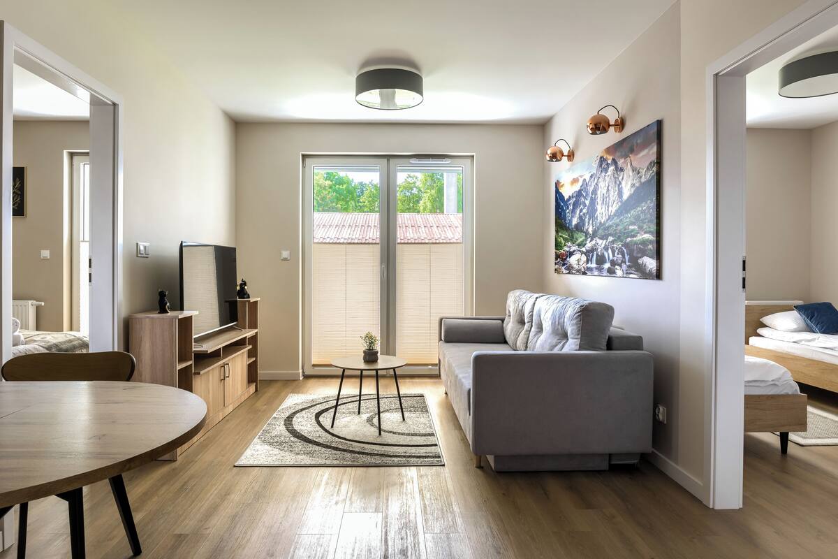 Una sala de estar moderna con un sofá gris, una mesa de comedor de madera y un televisor sobre un mueble de madera.