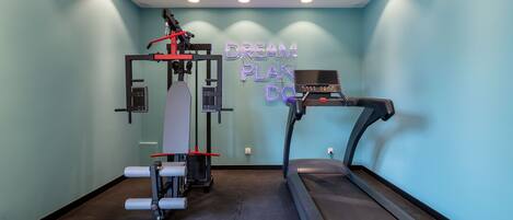 A gym with a treadmill and a weight machine, a neon sign on the wall, and a light blue wall.