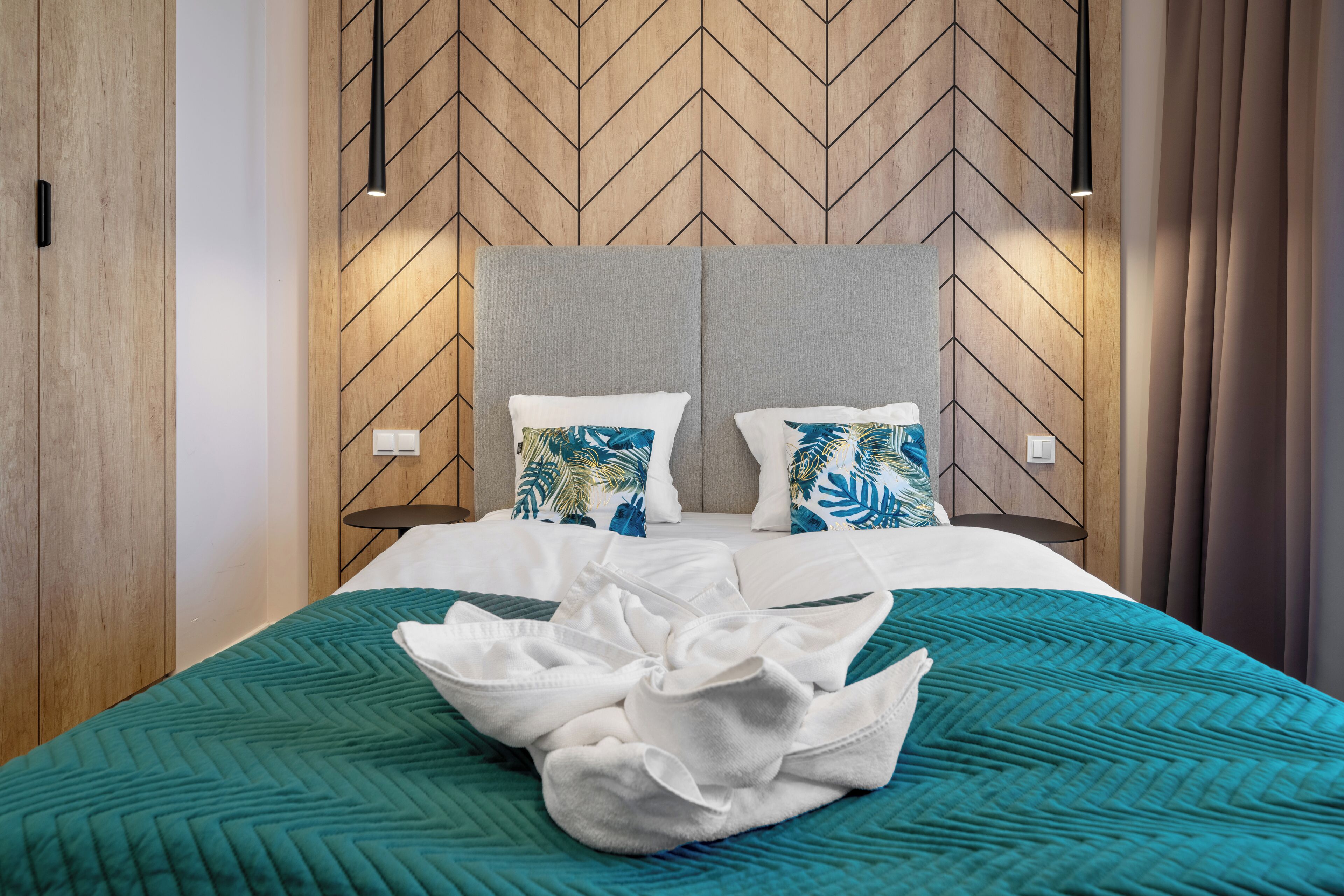 Ein Hotelzimmer mit Wänden aus Fischgrätparkett, einem grauen Stoffkopfende und einer lindgrünen gesteppten Bettdecke.