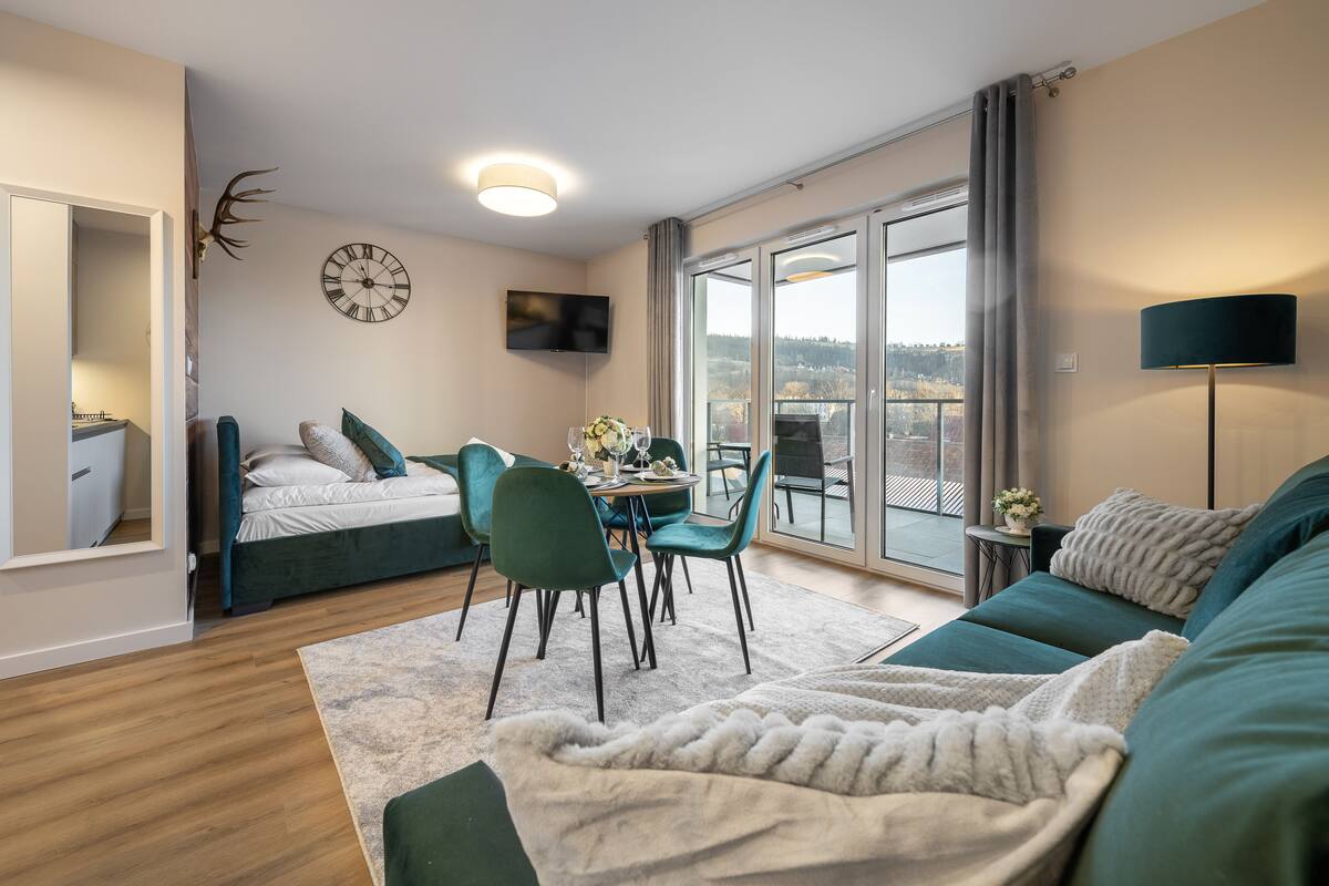 Una sala moderna con un sofá, una mesa de comedor con sillas, un televisor montado en la pared y un balcón con vistas.