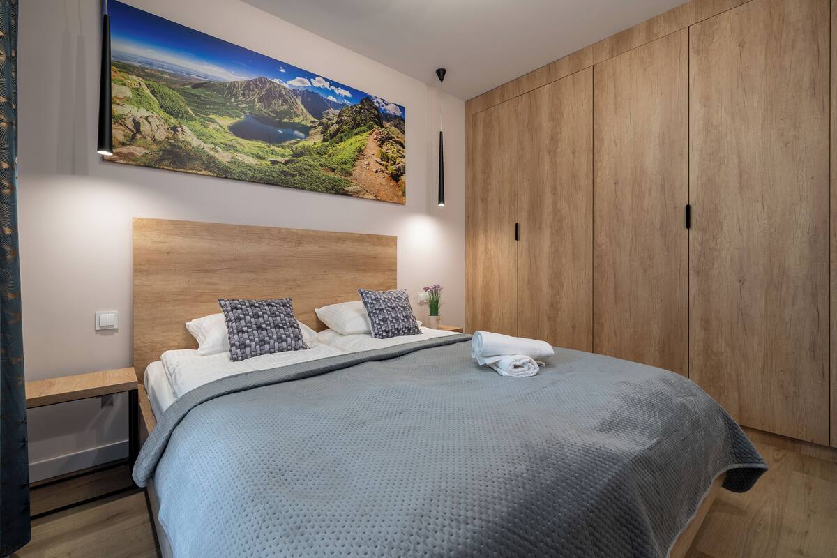 Un dormitorio con una cama grande, cabecera de madera, un cuadro de un paisaje y un armario.
