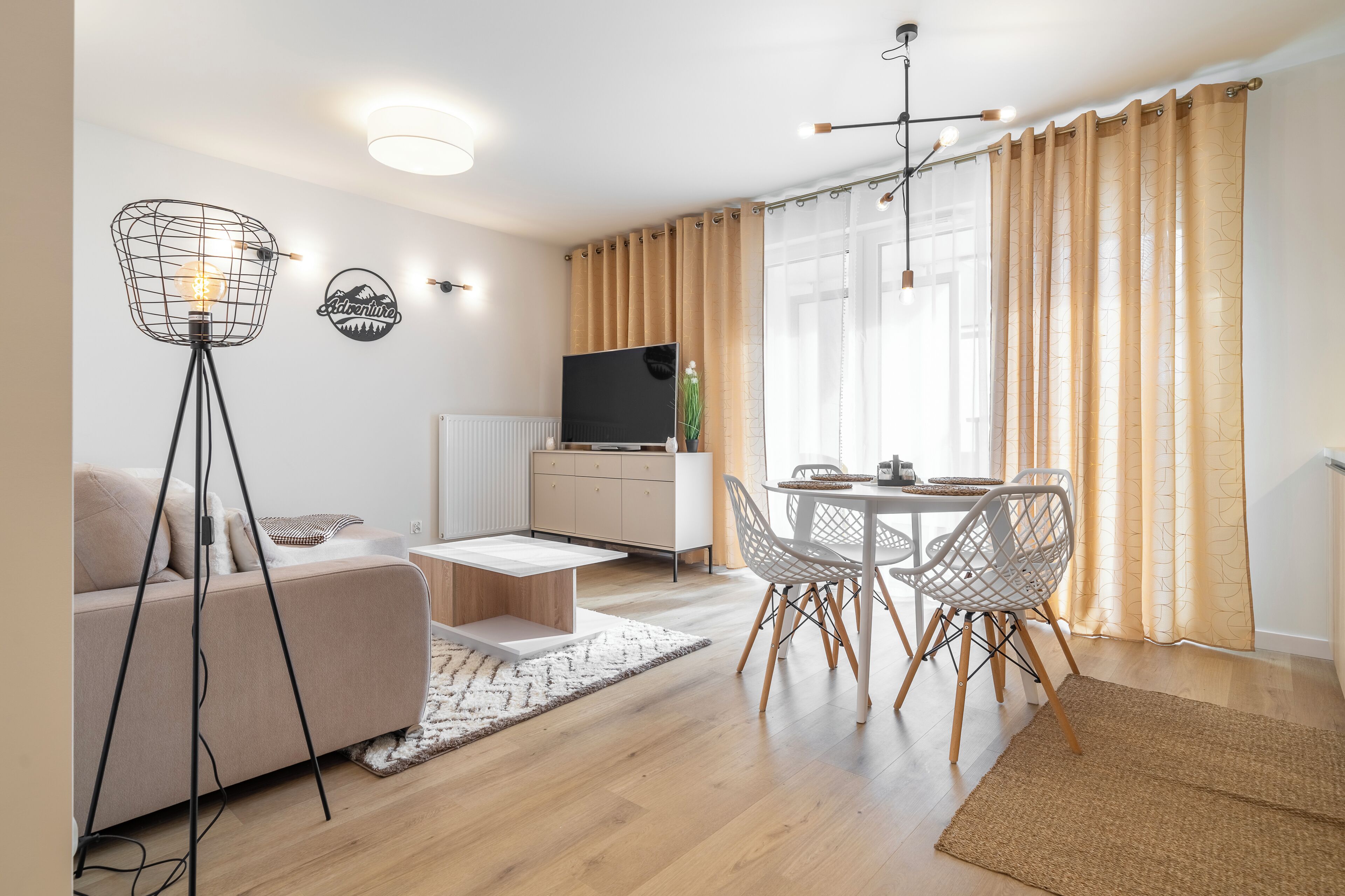 Ein modernes Wohnzimmer mit einer Couch, einem Esstisch, Stühlen, einem Fernseher und einer Stehlampe.