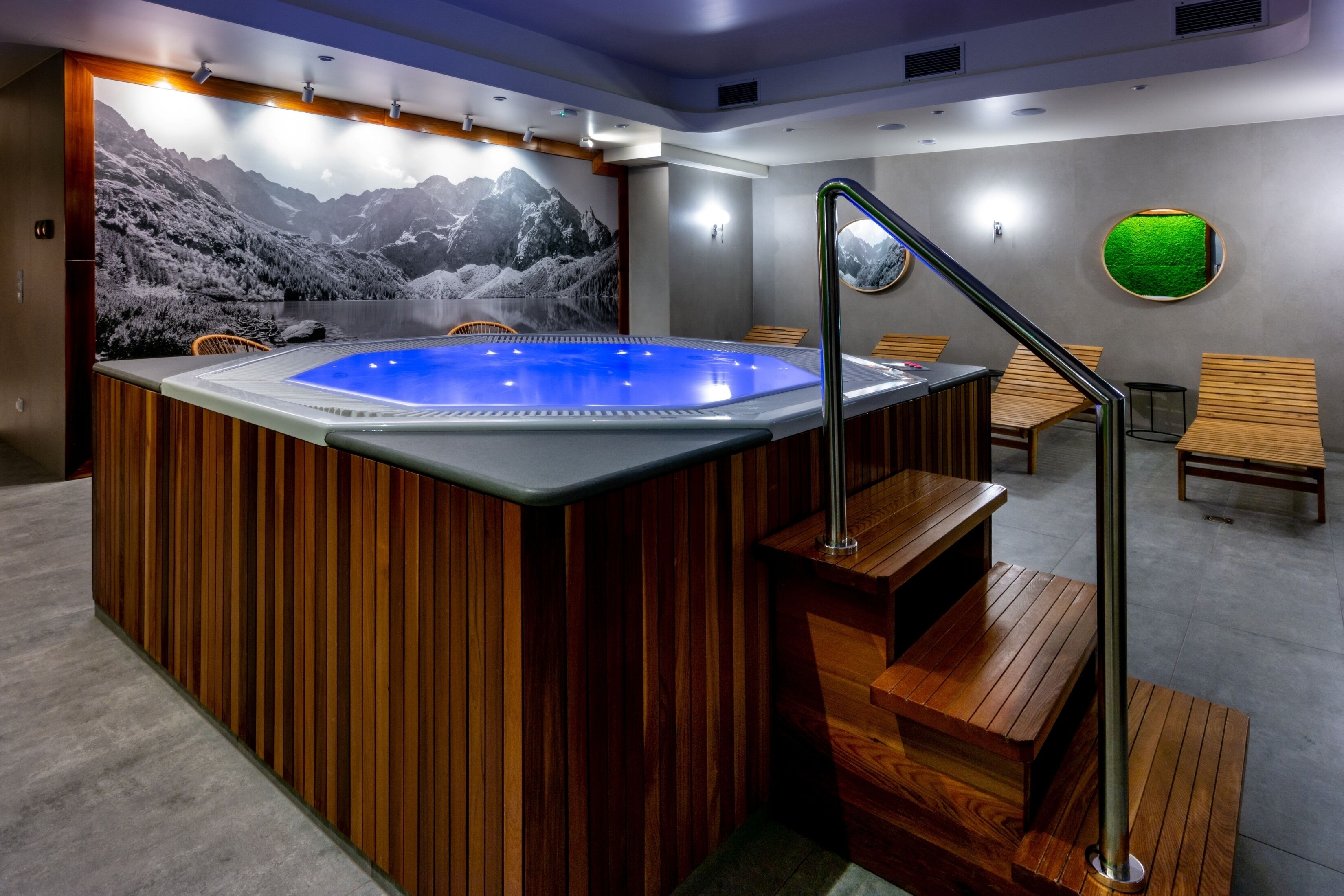 A modern spa area with a hot tub, wooden seating, and a mountain mural.