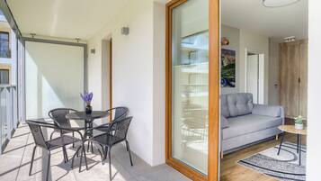 Una sala de estar moderna con un sofá gris, una mesa de comedor redonda con sillas y suelo de madera.