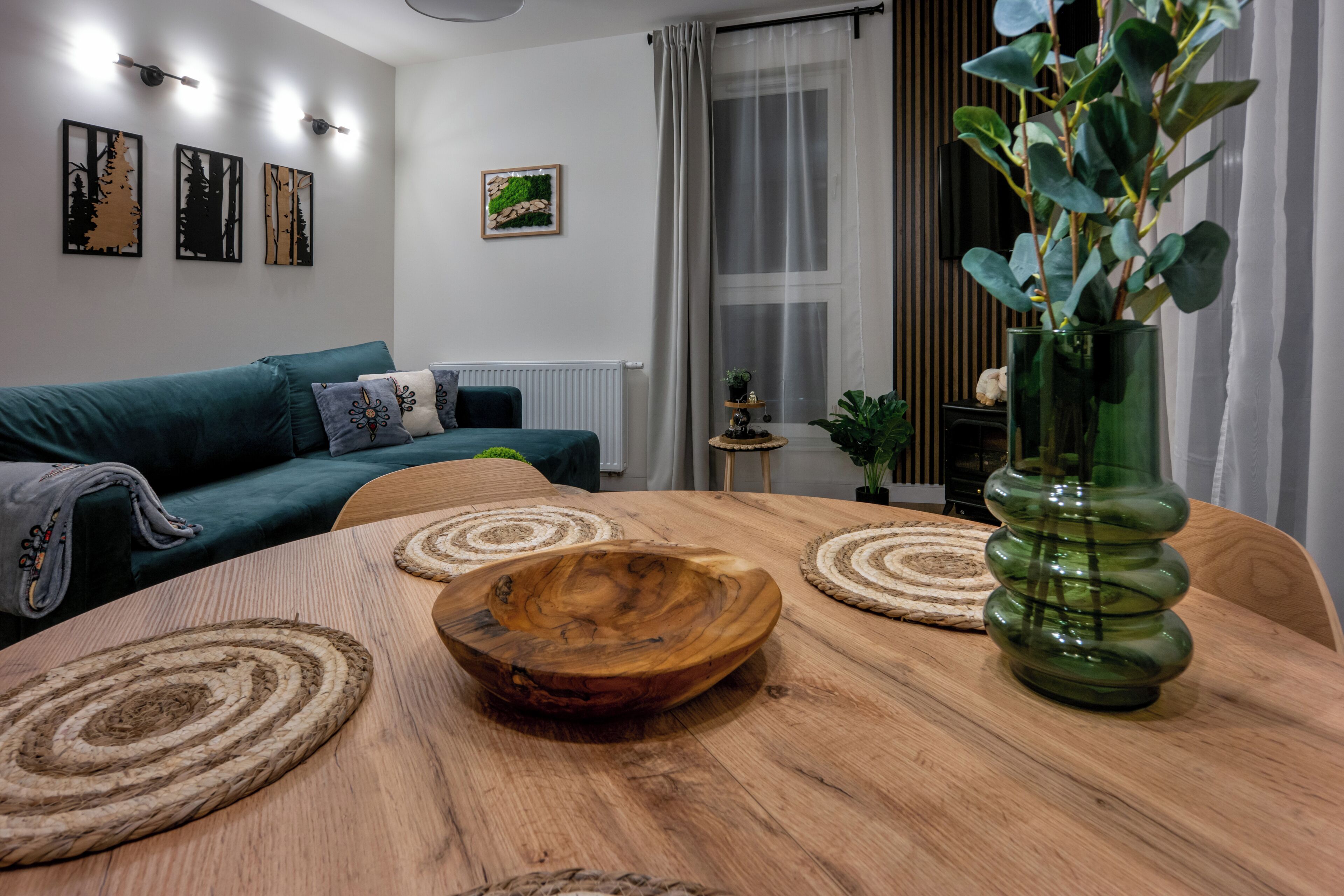 Una sala moderna con una mesa de madera, un jarrón verde y un sofá color turquesa.