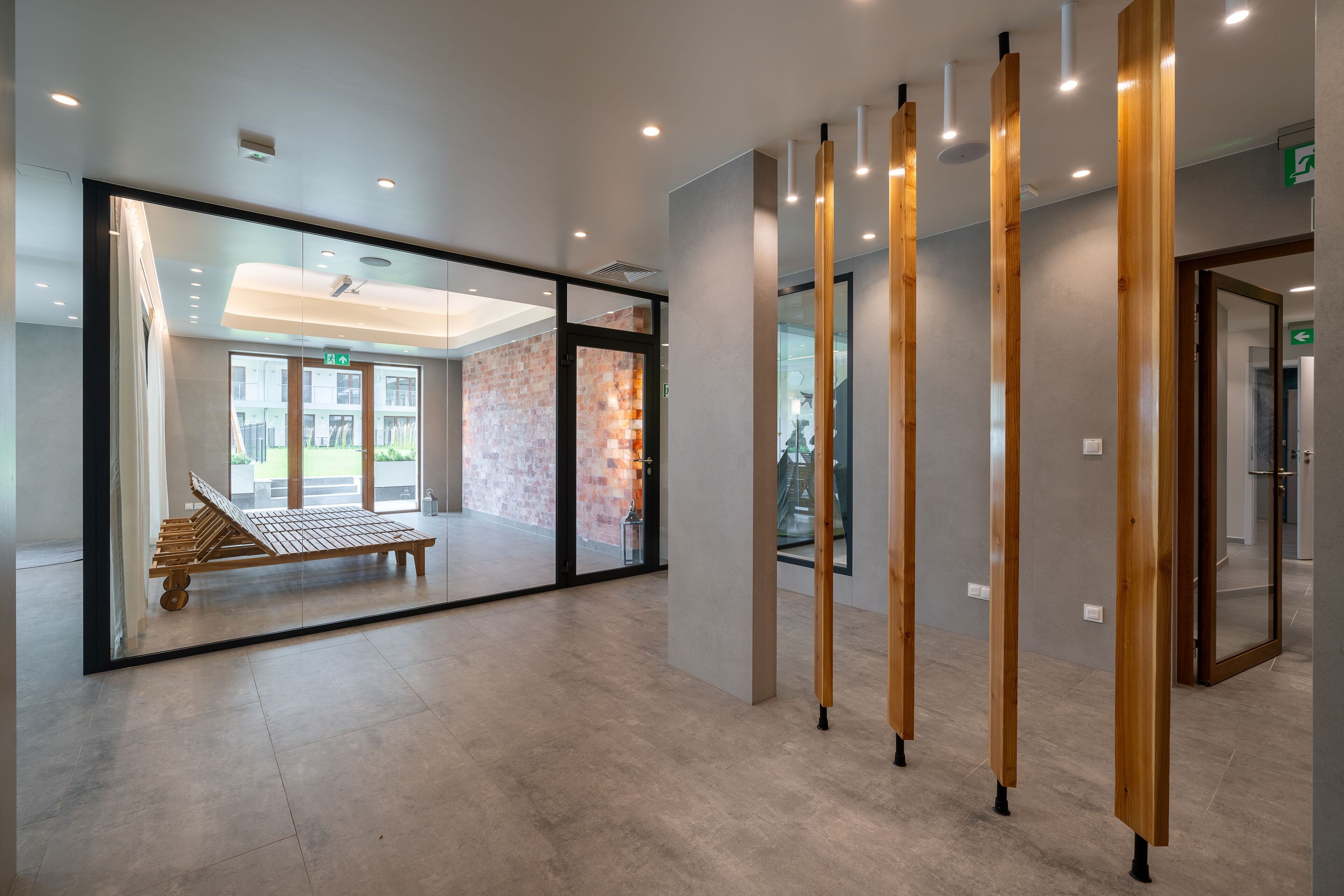 A modern hotel lobby with a glass partition, wooden benches, and a staircase.