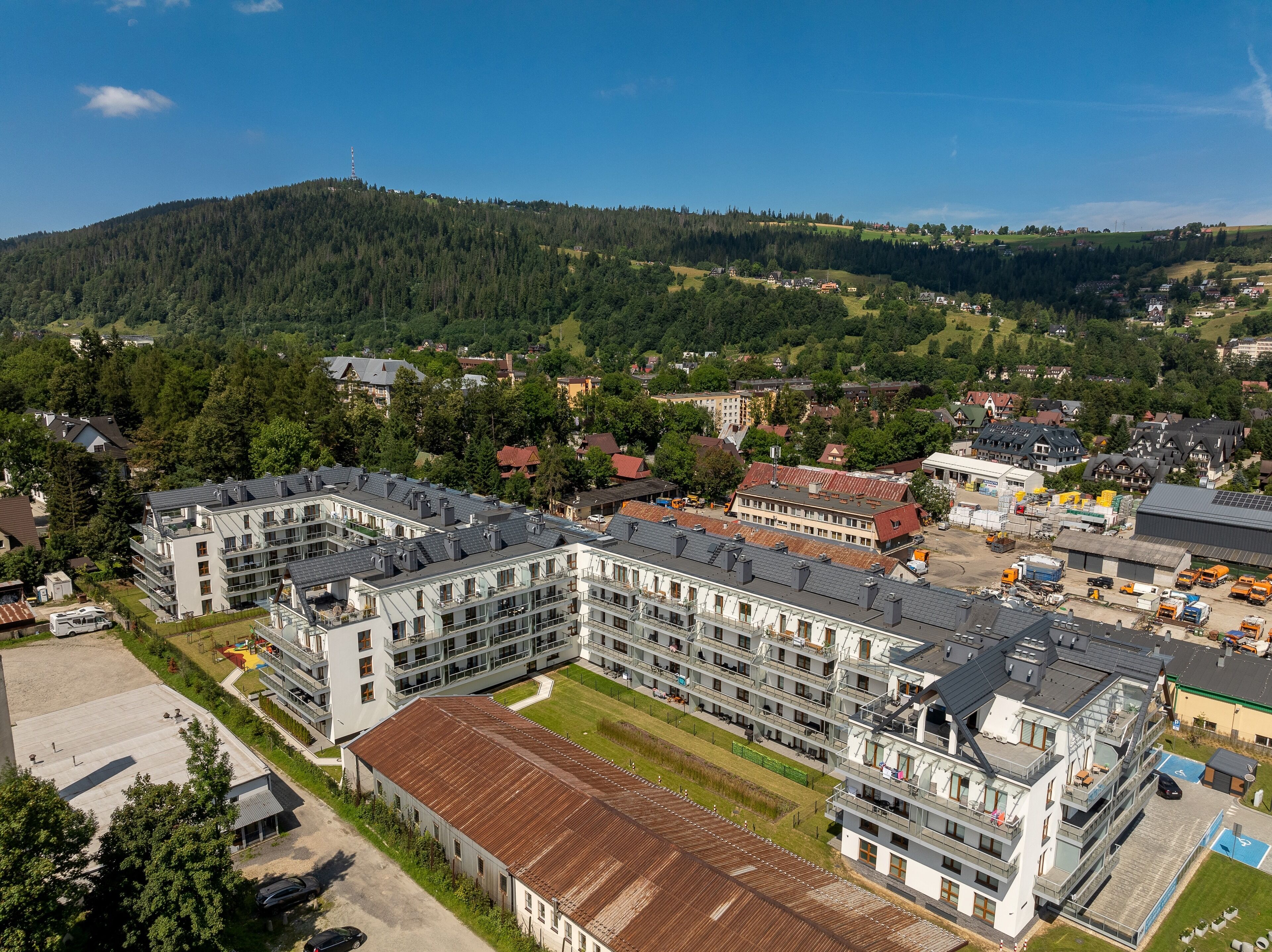 A multi-story hotel with a central courtyard, surrounded by residential buildings and a forested hill in the background.