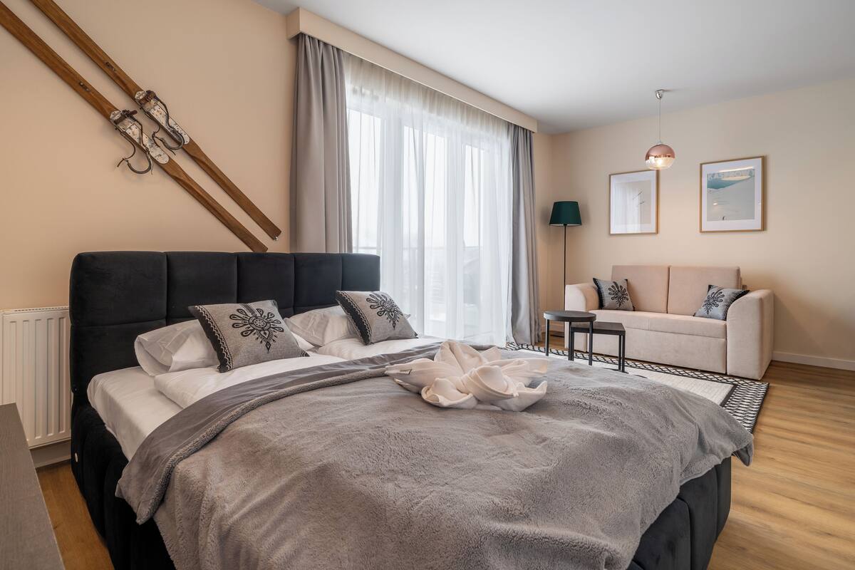 Un dormitorio con una cama grande, un sofá, una mesita y una ventana con cortinas.