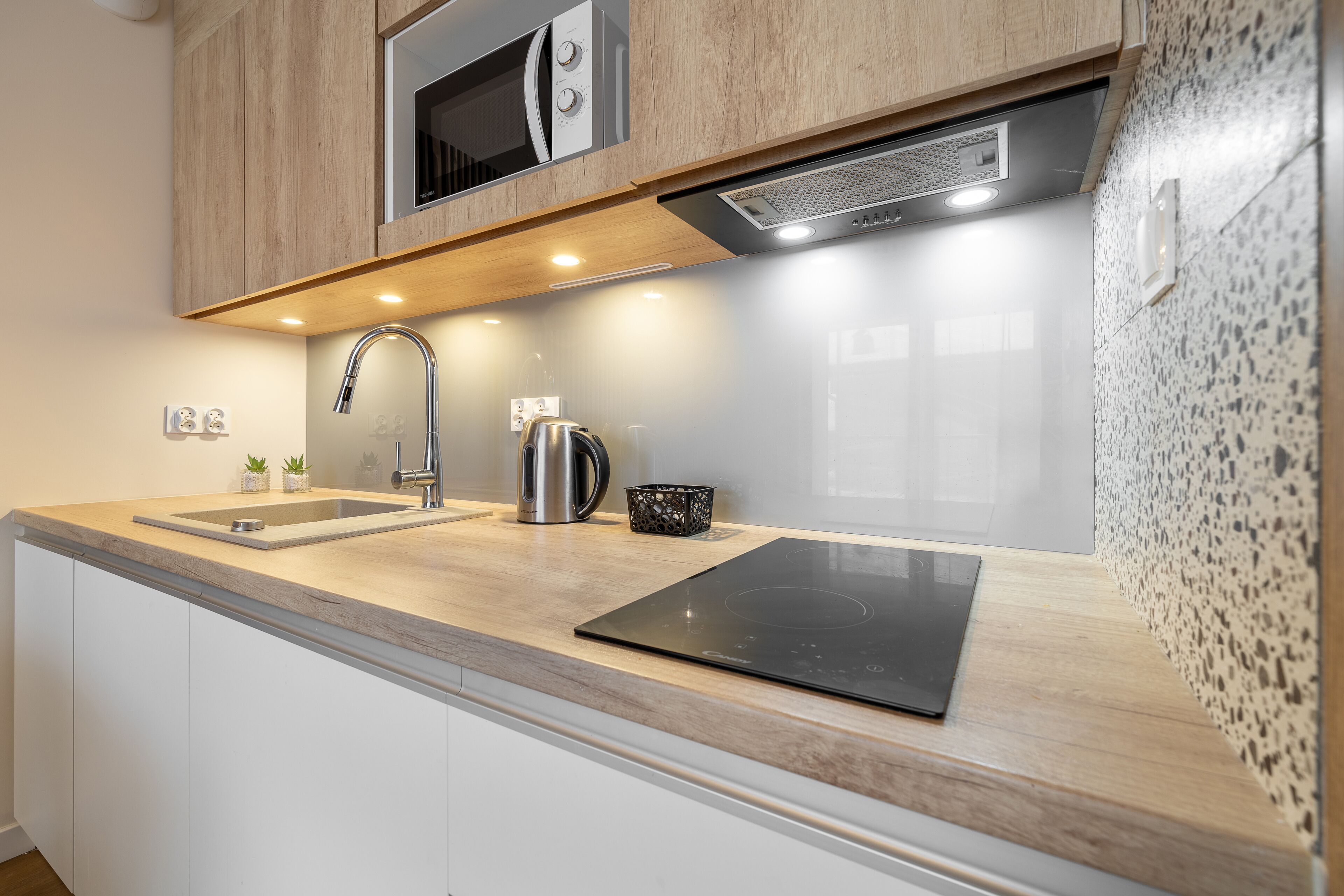 A modern kitchen with a stainless steel sink, a kettle, and a built-in stove.