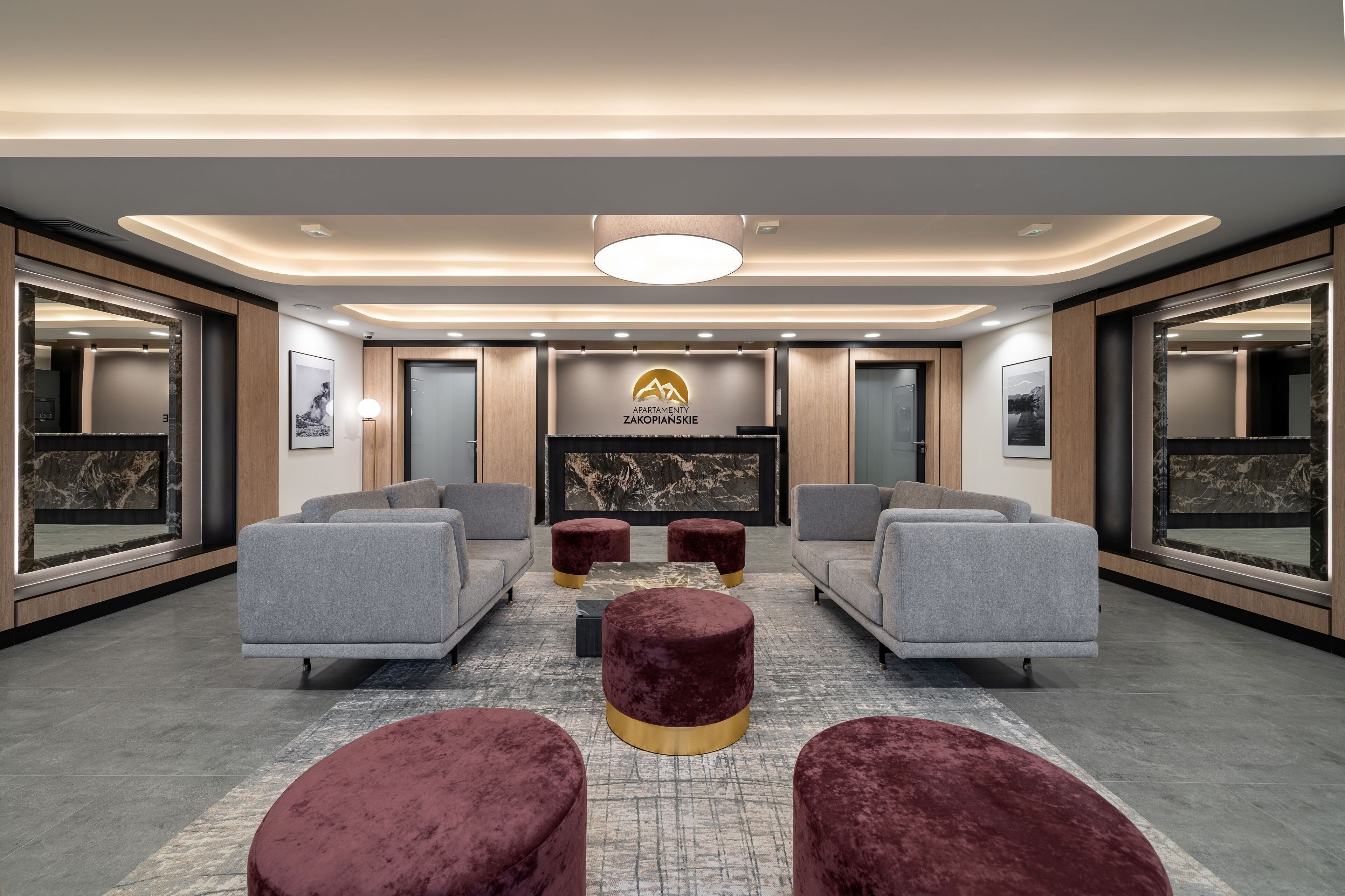 En modern entréhall med grå soffor, röda sittpallar och en centralt placerad öppen spis.