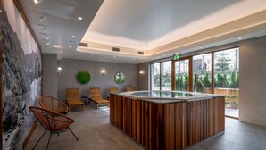 Uma área de recepção moderna com balcão de madeira, espaço para sentar e grandes janelas com vista para o exterior.