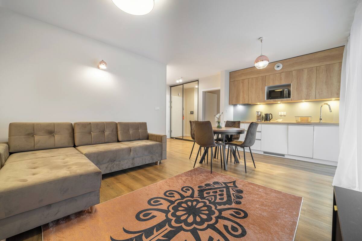 Una sala de estar moderna con un sofá, una mesa de comedor con sillas y una zona de cocina con armarios y un microondas.