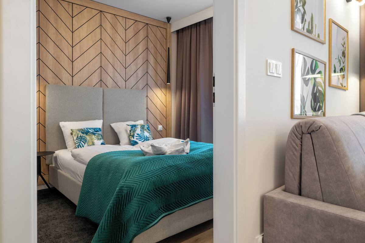Un dormitorio moderno con un cabecero de diseño geométrico, una cama con colcha color turquesa y un sillón tapizado en gris.