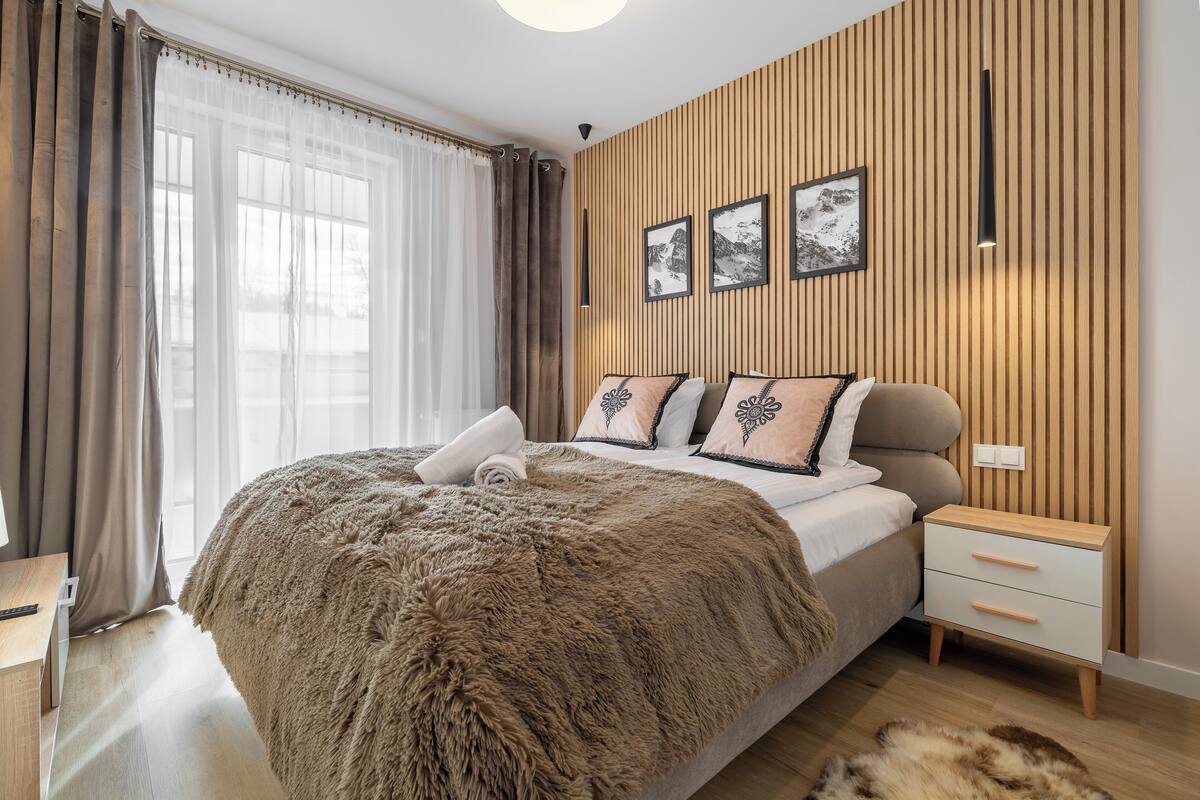 Un dormitorio moderno con una cama grande, un panel de pared de madera y una mesita de noche con lámpara.
