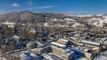 An aerial view of a snow-covered town with buildings, roads, and a forested mountain in the background.