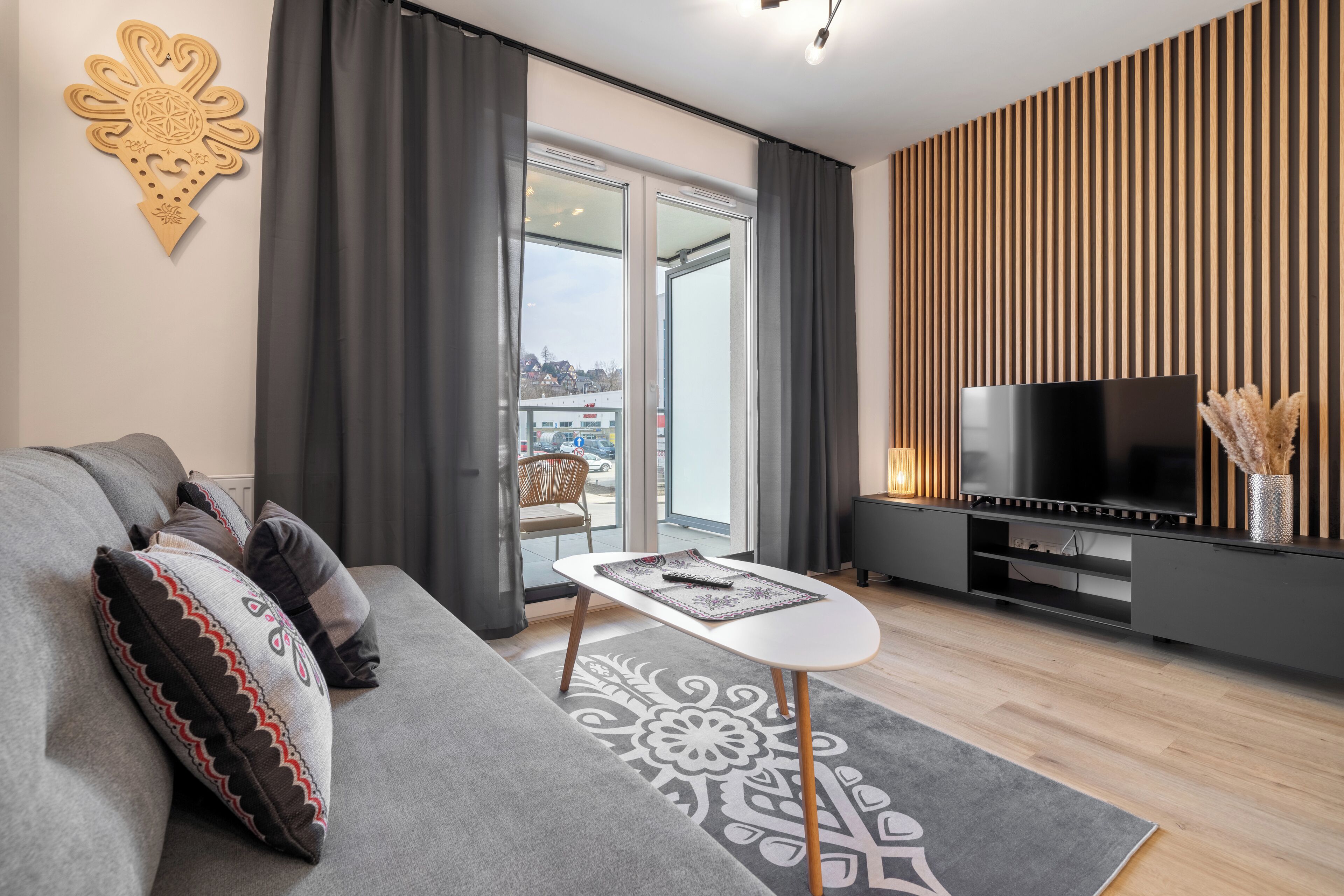 A modern living room with a sofa, a small table, a TV, and a sliding glass door leading to a balcony.