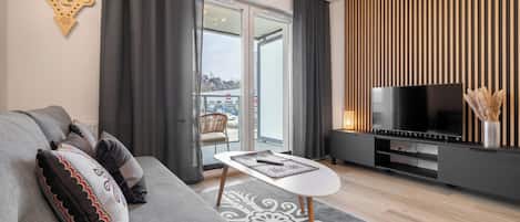 A modern living room with a sofa, a small table, a TV, and a sliding glass door leading to a balcony.