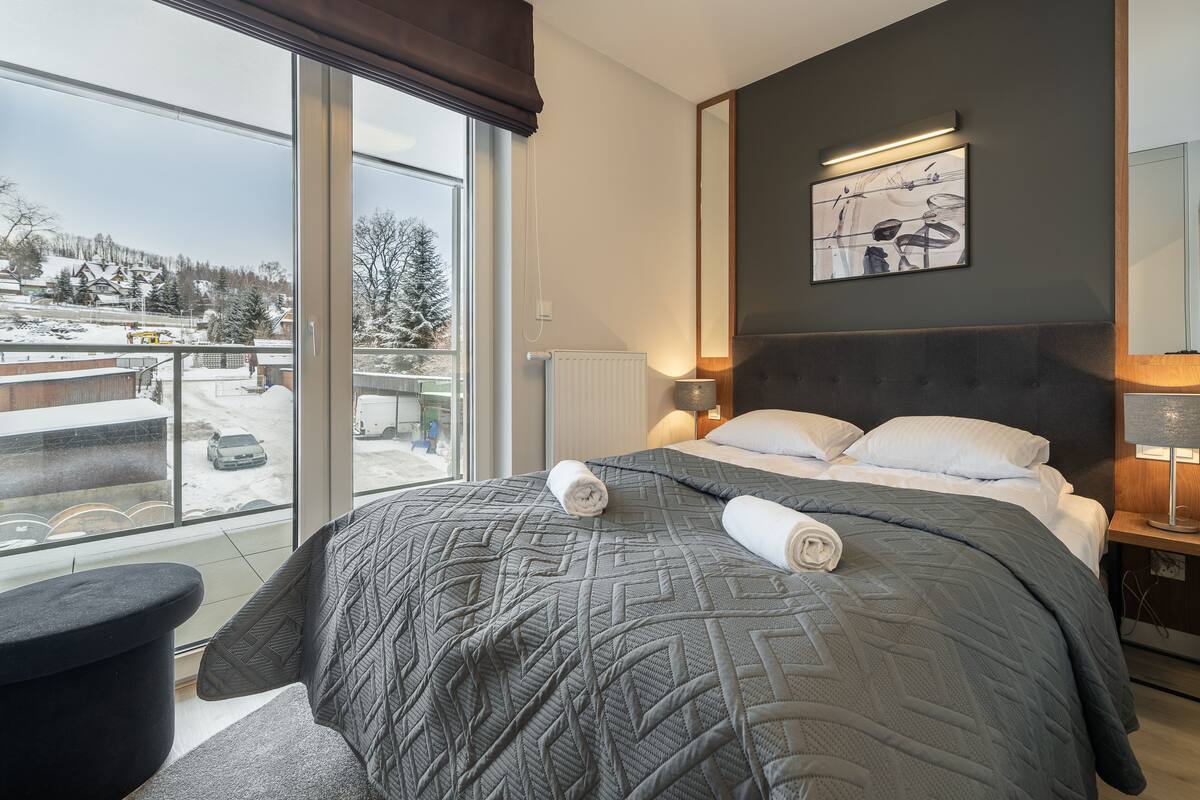 Habitación de hotel moderna con una cama grande, vistas a un paisaje nevado y una obra de arte contemporánea en la pared.