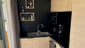 Une cuisine compacte avec des meubles de rangement en bois, un plan de travail noir, un four à micro-ondes et un évier.