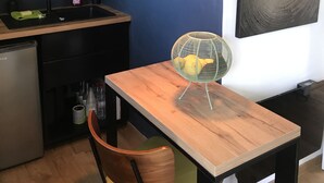 Una cucina moderna con mobili scuri, un piano di lavoro in legno, una lampada a sospensione e un'area pranzo con una sedia e un tavolo.