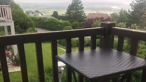 Un'area esterna con un ponte in legno, un tavolo in metallo e due sedie, ognuna con un cuscino giallo.