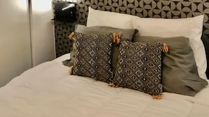 Un letto rifatto con cuscini decorati, un ornamento solare a parete e carta da parati con motivo geometrico.