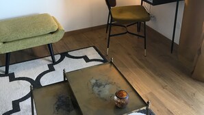 Una stanza con una scrivania, una sedia e un piccolo tavolo con un oggetto decorativo. Si nota una libreria con diversi oggetti e una lampada sulla scrivania.